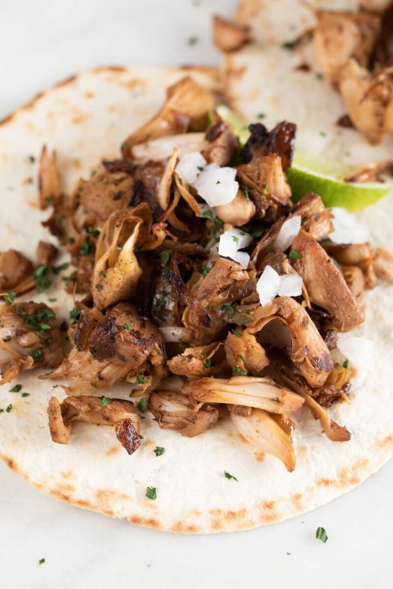 Close-up photo of a jackfruit carnita with a lemon wedge, chopped cilantro and diced onion