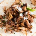 Close-up photo of a jackfruit carnita with a lime wedge, chopped cilantro and diced onion with a heading