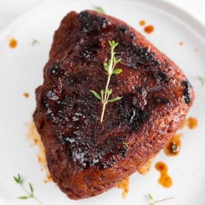 Vegan steak presented on a white plate, garnished with fresh thyme.