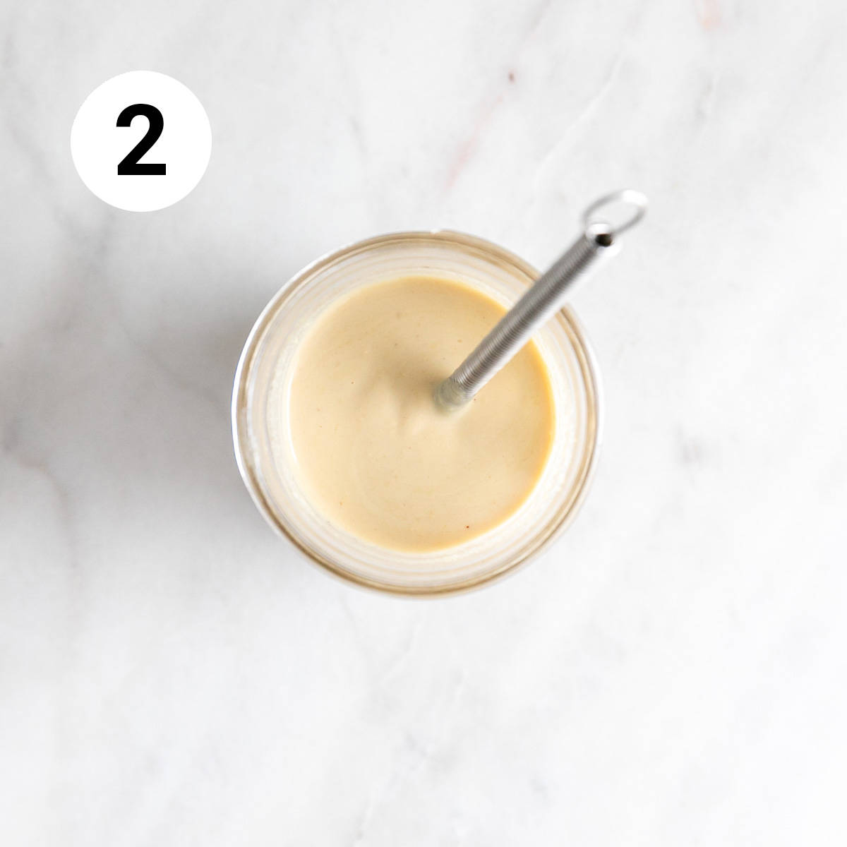 Jar with lemon tahini dressing and a small whisk.