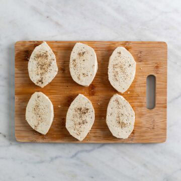 6 tofu filets seasoned with salt and pepper on a wooden cutting board.