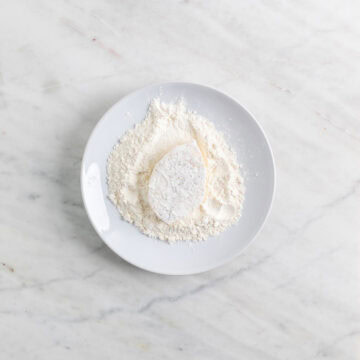 Tofu filet being coated in flour on a plate.