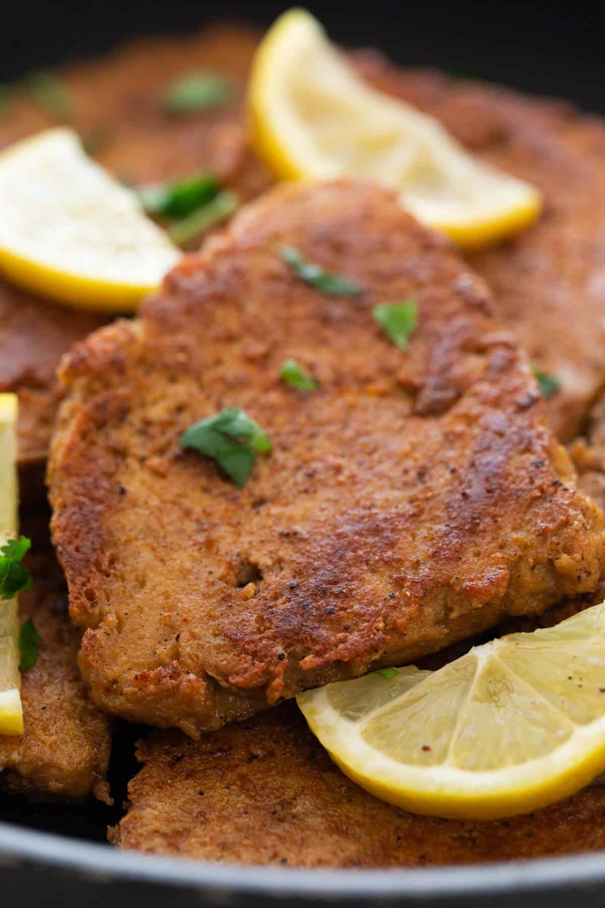 Several vegan chicken fillets in a skillet with some chopped cilantro and lemon slices on top.