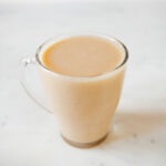 A square picture of a glass with homemade rice milk and some brown rice around