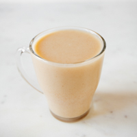 A square picture of a glass with homemade rice milk and some brown rice around