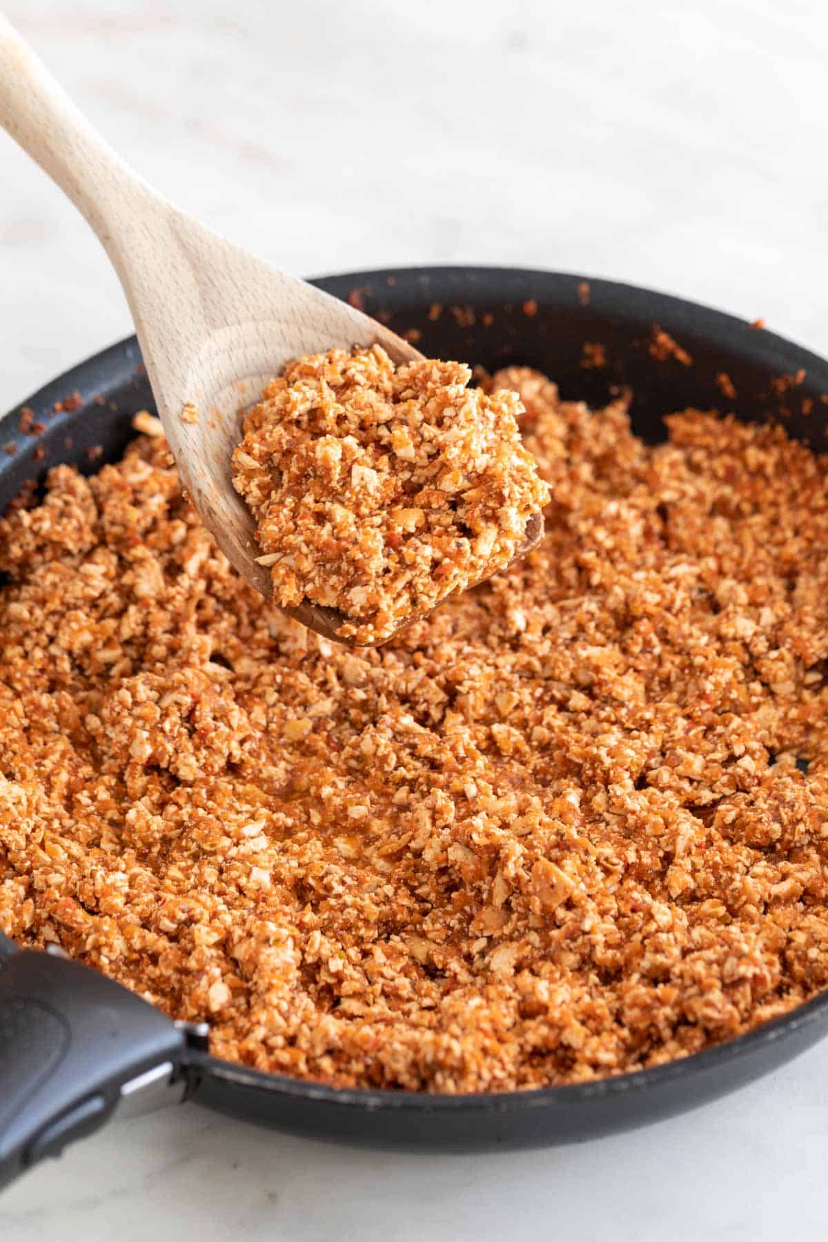 A wooden spoon with some Chipotle sofritas and a frying pan with the remaining sofritas.