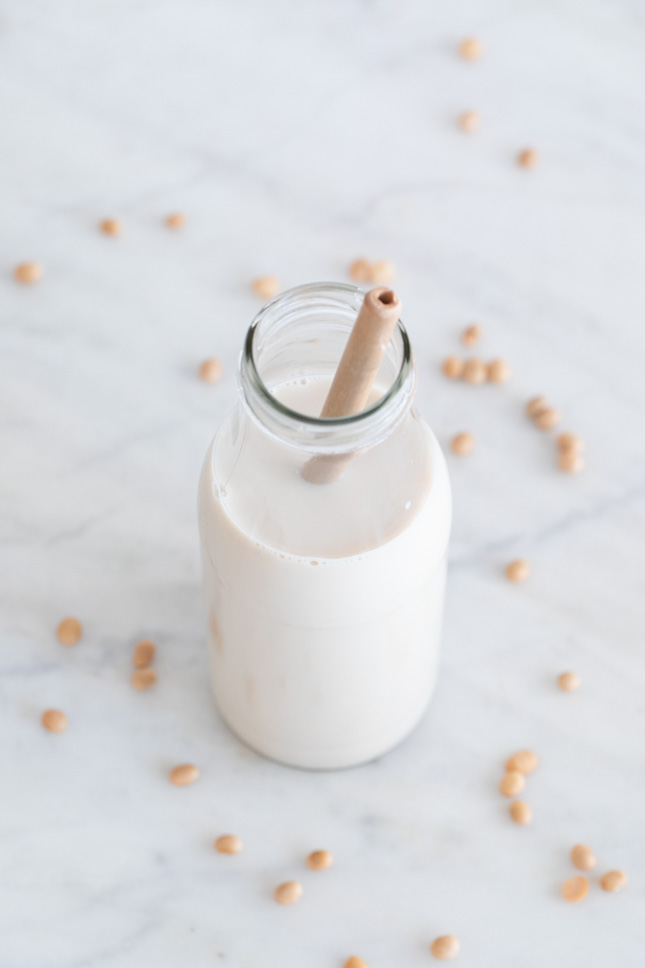 A shot of a glass with homemade soy milk and a bamboo straw