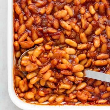 Vegan baked beans displayed in a casserole dish alongside a spoon.