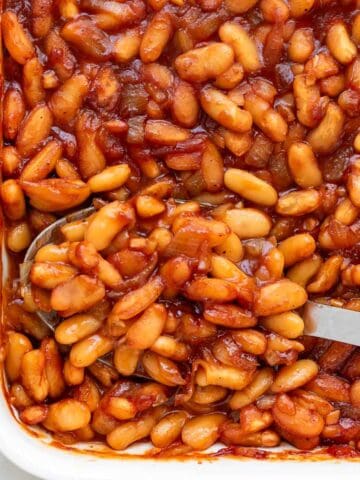 Vegan baked beans displayed in a casserole dish alongside a spoon.
