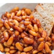 Vegan baked beans served in a bowl alongside a piece of bread.