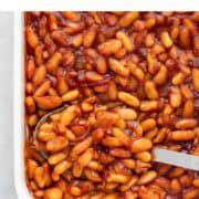 Vegan baked beans in a baking dish with a spoon.