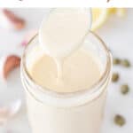 Spoon pouring vegan Caesar dressing onto a mason jar with ingredients in the background.