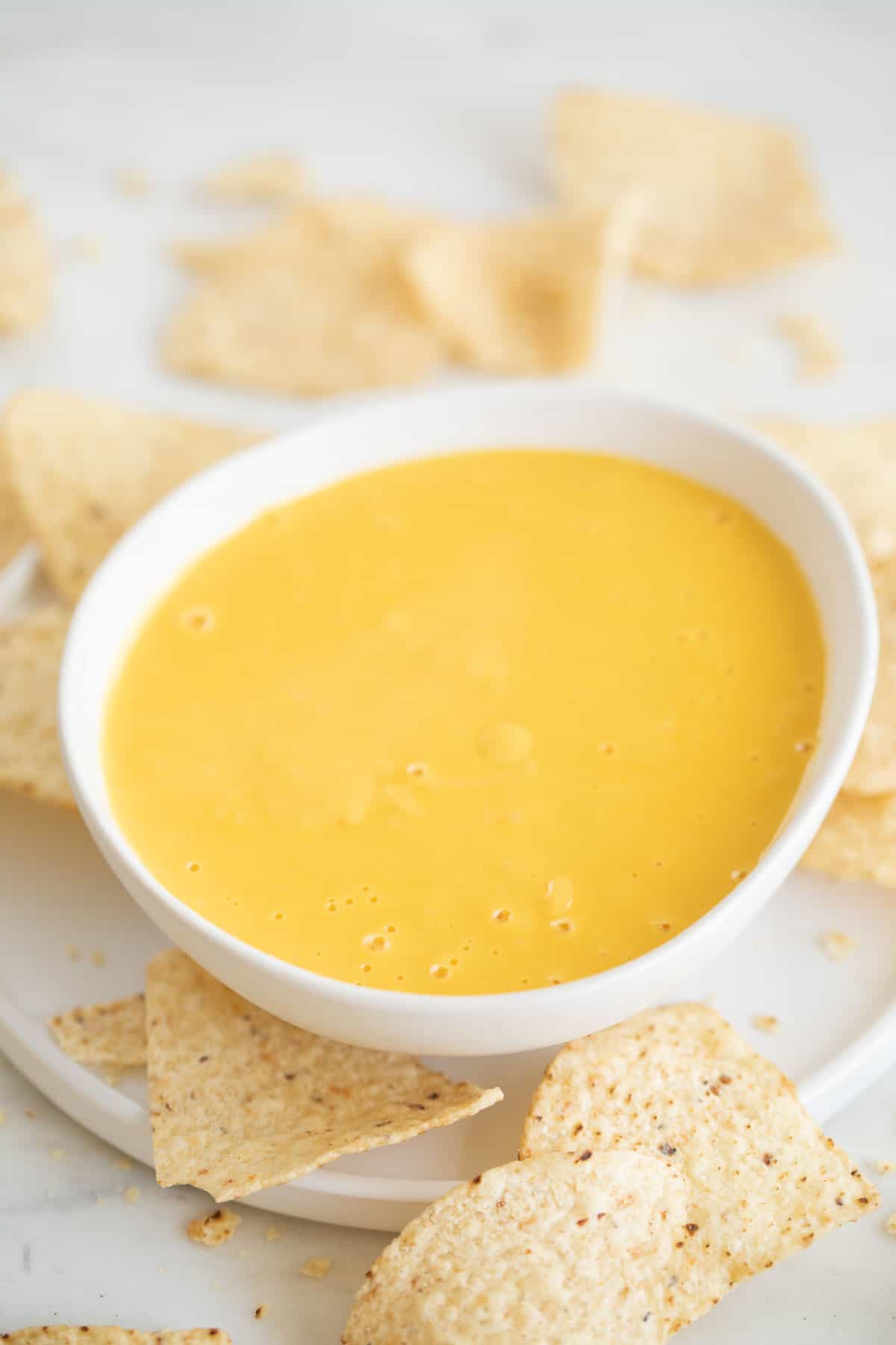 White bowl of vegan cheese surrounded by tortilla chips.