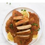 A dish with some vegan chicken fillets, one of them sliced, with some chopped cilantro and lemon slices on top.