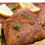 Several vegan chicken fillets in a skillet with some chopped cilantro and lemon slices on top.