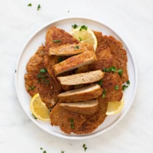 A dish with some vegan chicken fillets, one of them sliced, with some chopped cilantro and lemon slices on top.