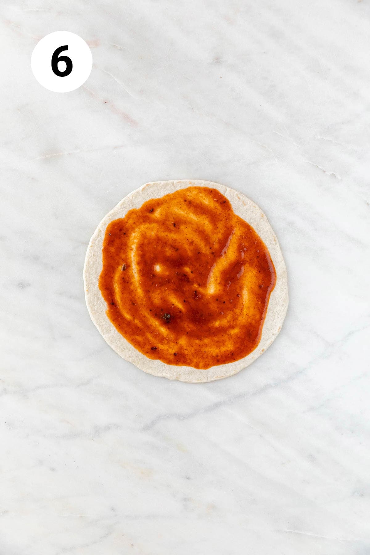 Red enchilada sauce spread onto a flour tortilla.
