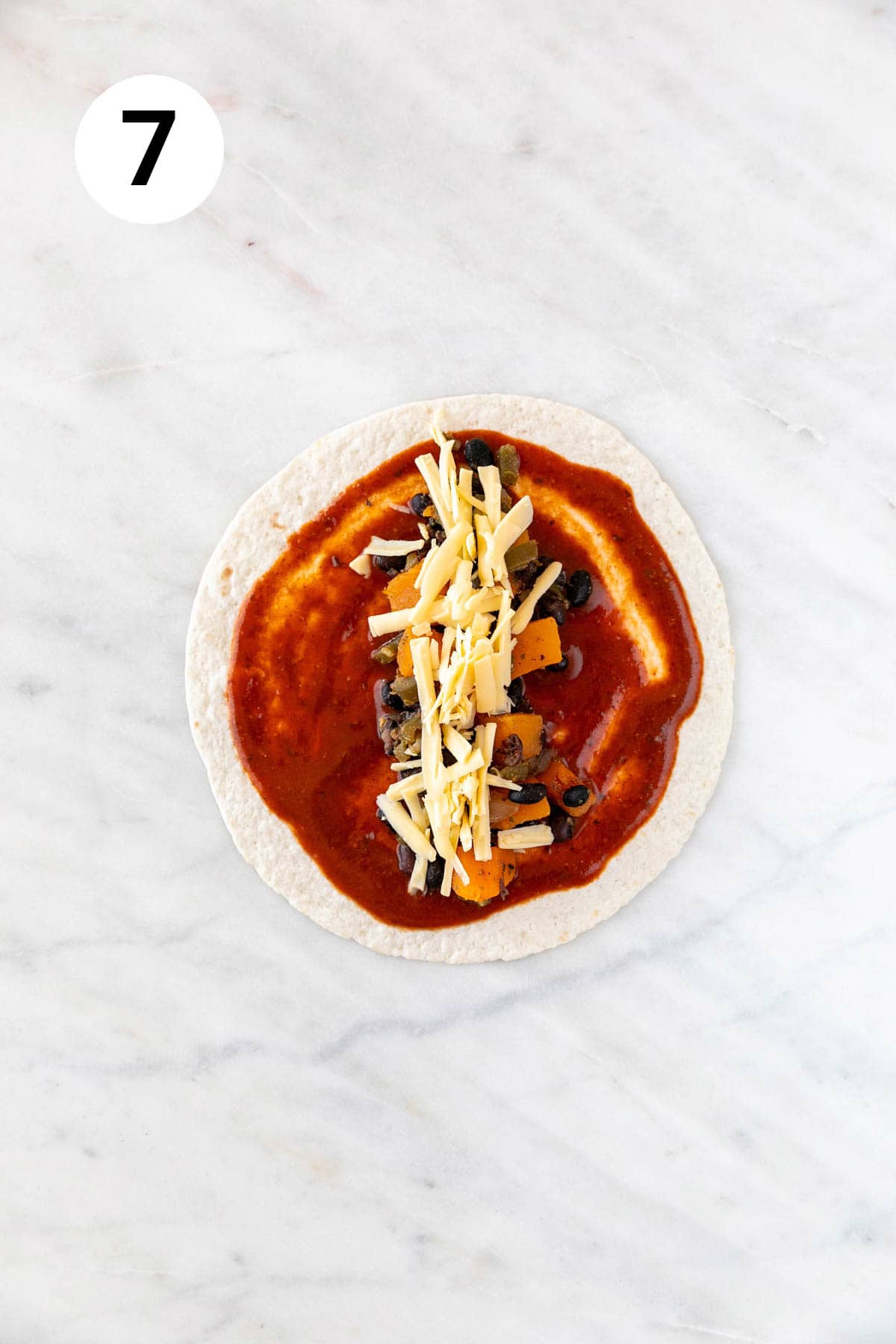 "A tortilla smeared with red enchilada sauce, filled with enchilada filling and vegan cheese.
