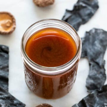 Jar of vegan fish sauce with seaweed and dried mushrooms in the background.