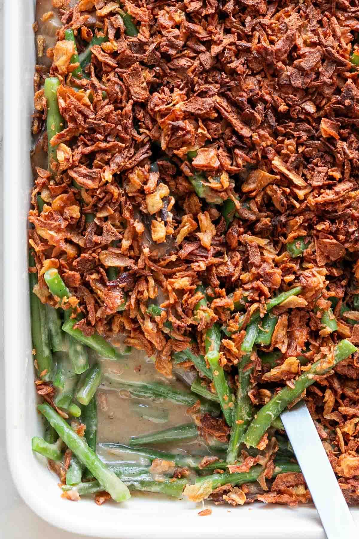 Baking dish of vegan green bean casserole with a serving spoon.