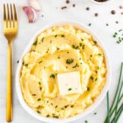 Bowl of vegan mashed potatoes garnished with vegan butter, chives, black pepper, and a fork on the side.