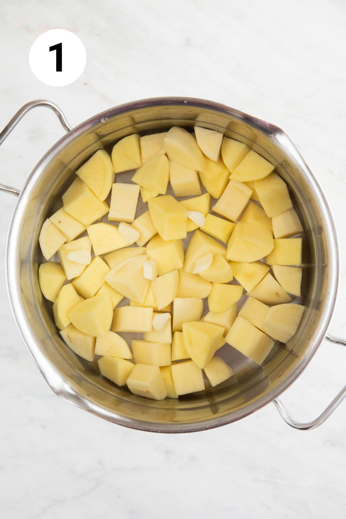 Large pot with cubed potatoes and sliced garlic cloves covered with water just before cooking.