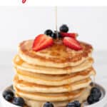 Vegan pancakes stacked high with strawberries, blueberries, and a drizzle of maple syrup.