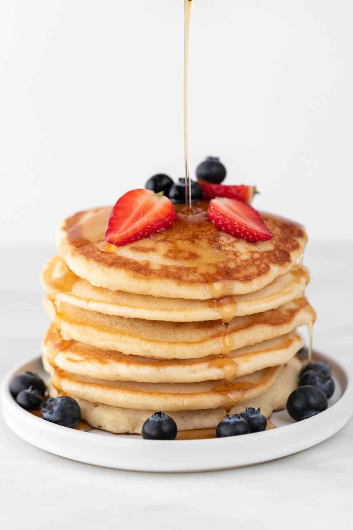 Stack of vegan pancakes topped with strawberries, blueberries, and a maple syrup drizzle.