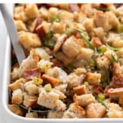 Vegan stuffing in baking dish with serving spoon and fresh rosemary.