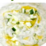 Bowl of vegan tzatziki sauce topped with cucumber and drizzled with olive oil.