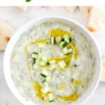 Vegan tzatziki sauce bowl with background of pita bread and garlic cloves.
