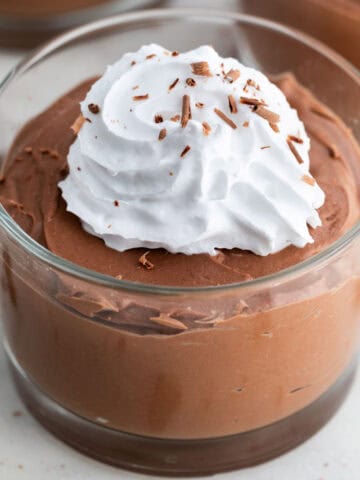 Three serving glasses of tofu chocolate mousse topped with vegan whipped cream and chocolate shavings.
