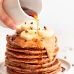 Stack of vegan banana pancakes topped with peanut butter, chocolate chips, banana, and syrup.