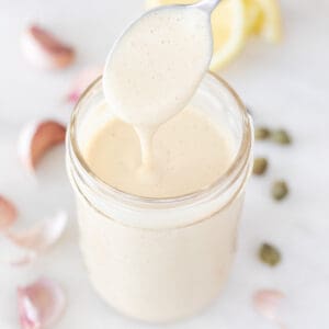 Drizzling vegan Caesar dressing onto a mason jar with ingredients in the background.