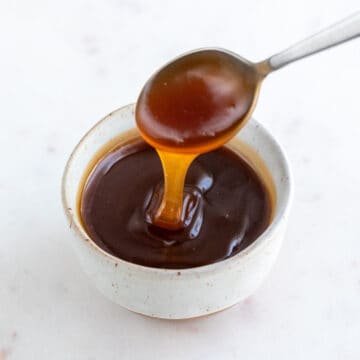 Dipping spoon into bowl of vegan caramel sauce.