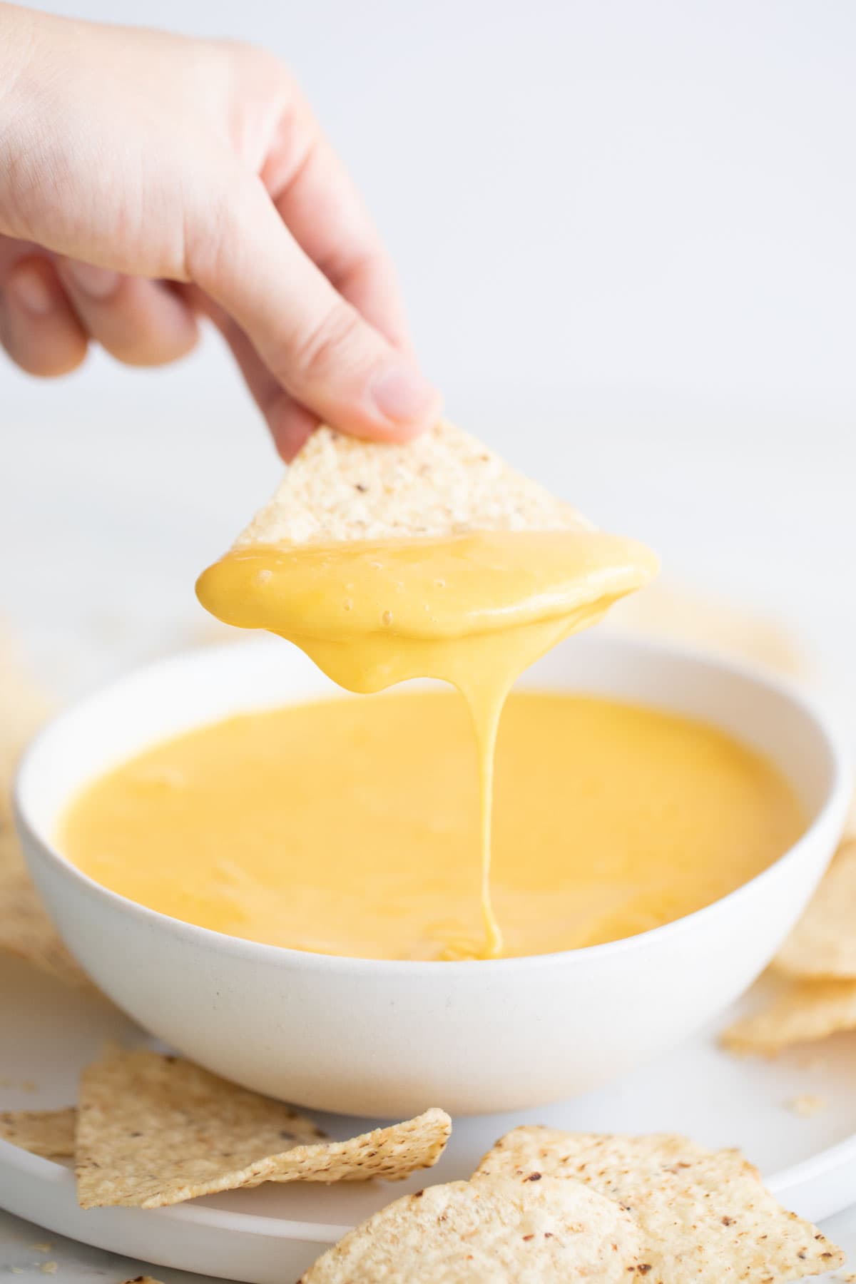 Hand dipping a tortilla chip into vegan cheese.