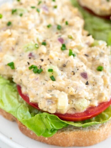 Sliced bread topped with lettuce, tomato, and vegan chicken salad.