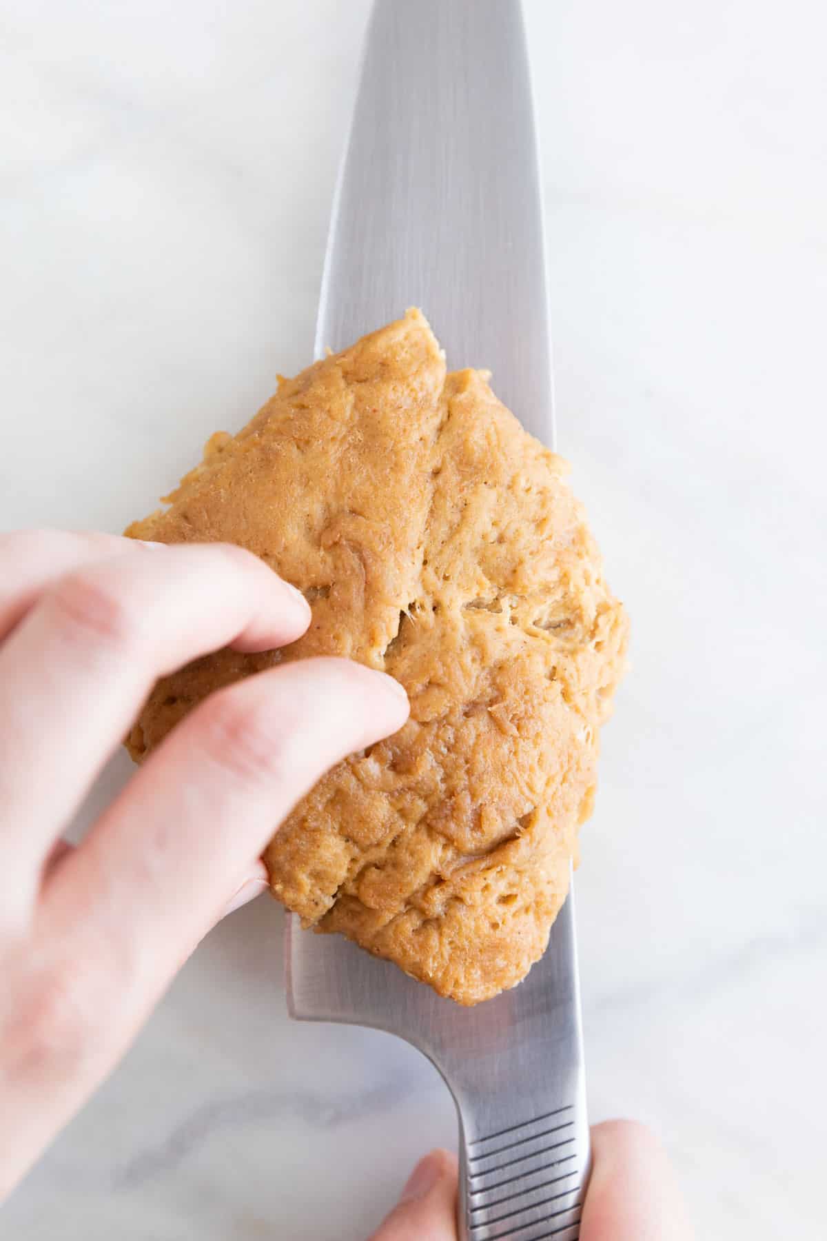 A hand cutting a piece of vegan chicken lengthways down the middle.