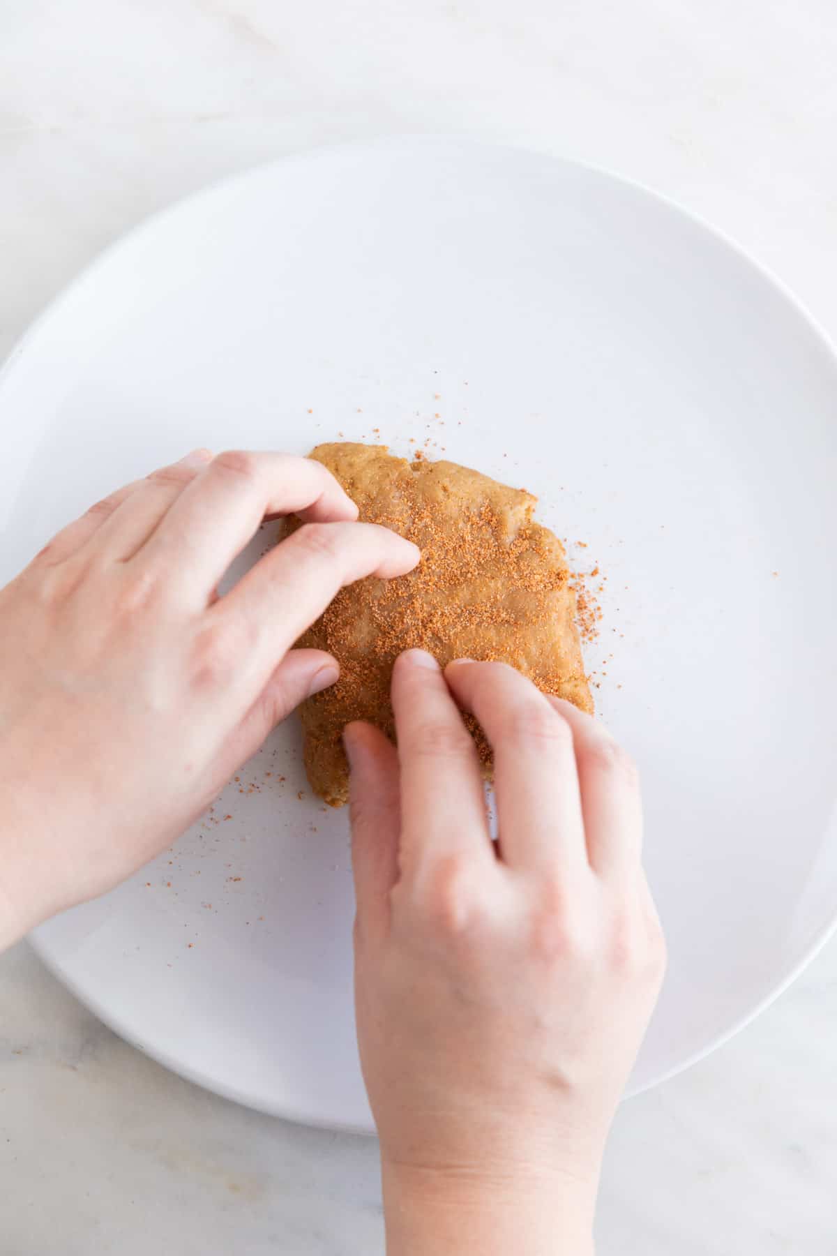 Two hands Sprinkle the extra chicken seasoning onto the fillets and rubbing some chicken seasoning into a chicken fillet.