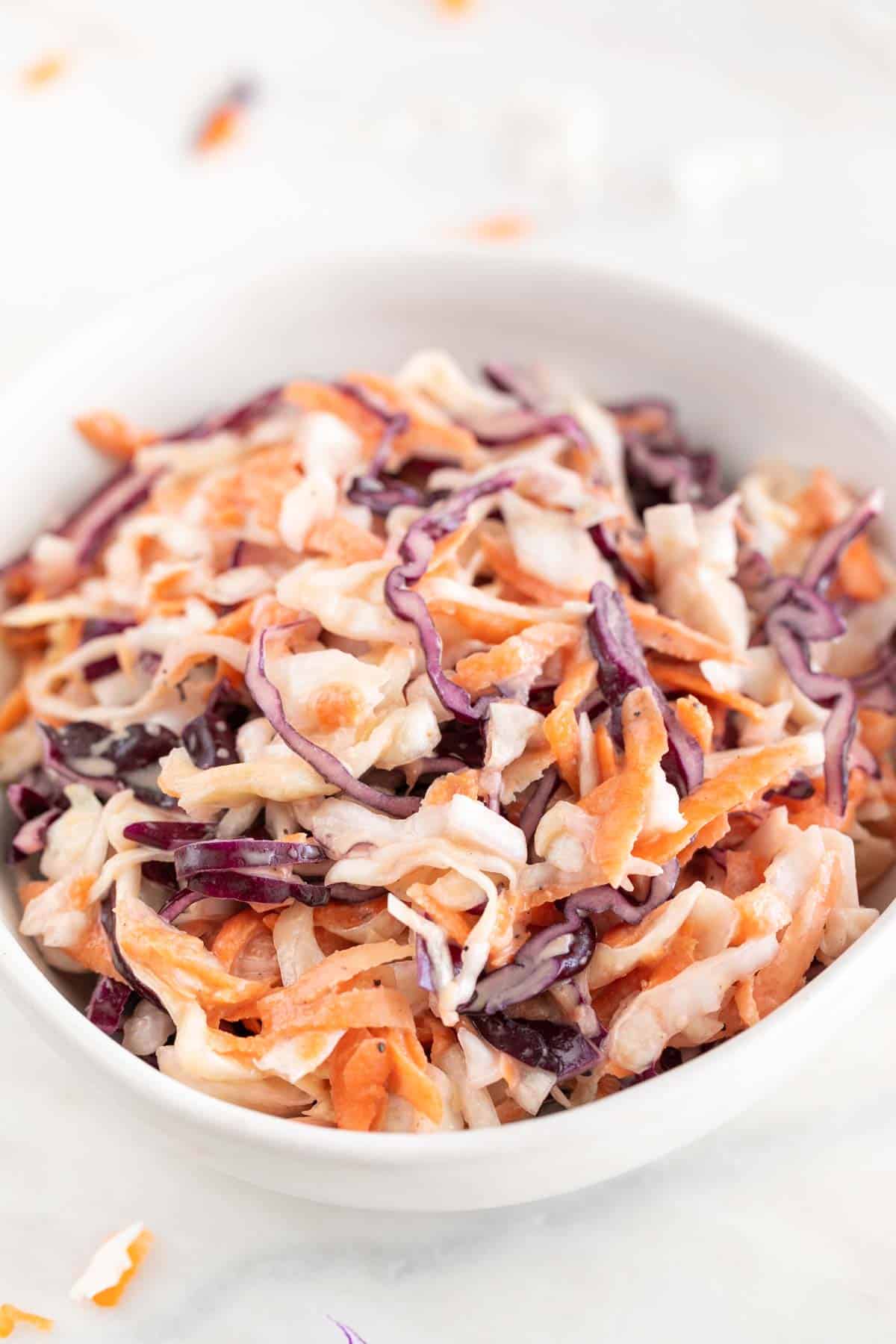White bowl with vegan coleslaw on a marble background.