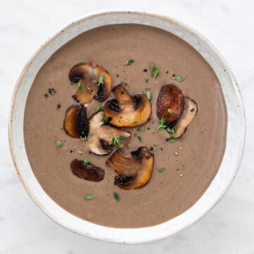 Bowl of creamy mushroom soup topped with black pepper, fresh thyme, and sautéed mushrooms.