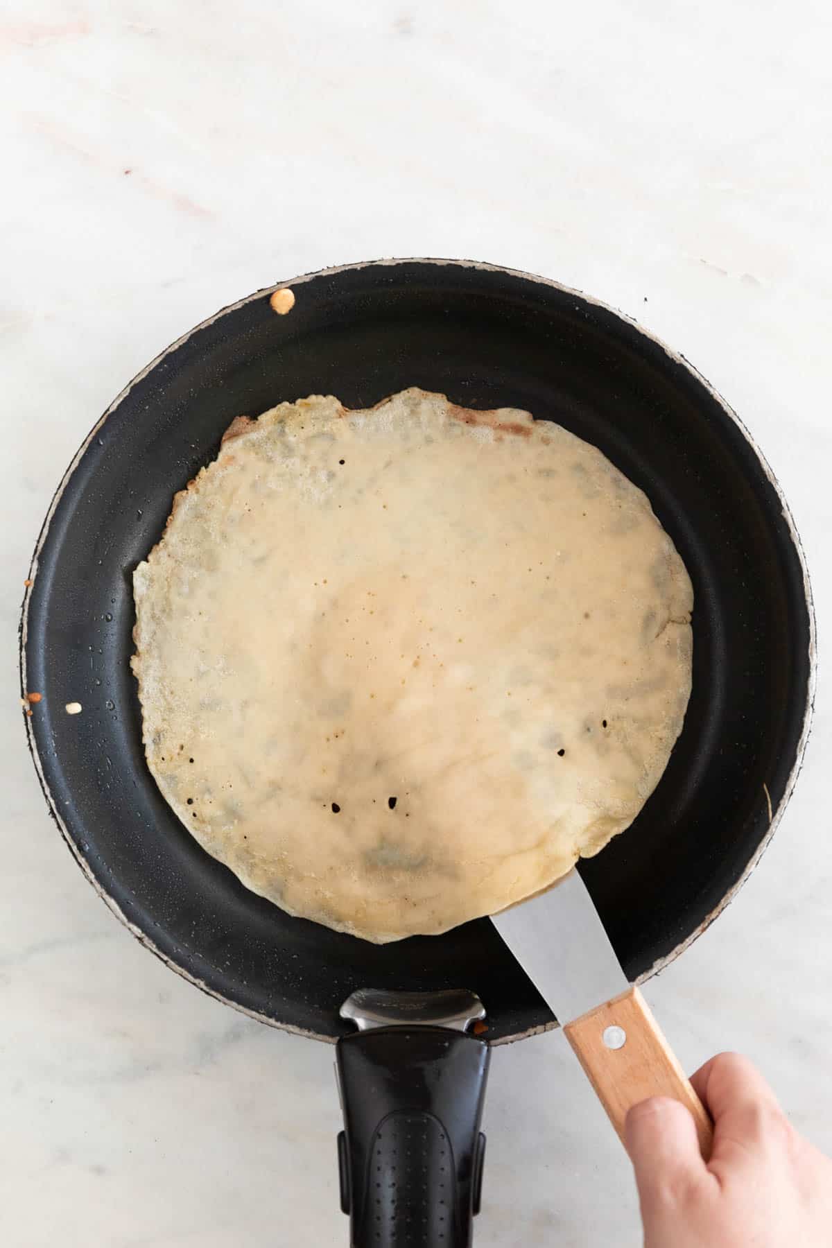 A hand with a butter knife flipping a crepe.