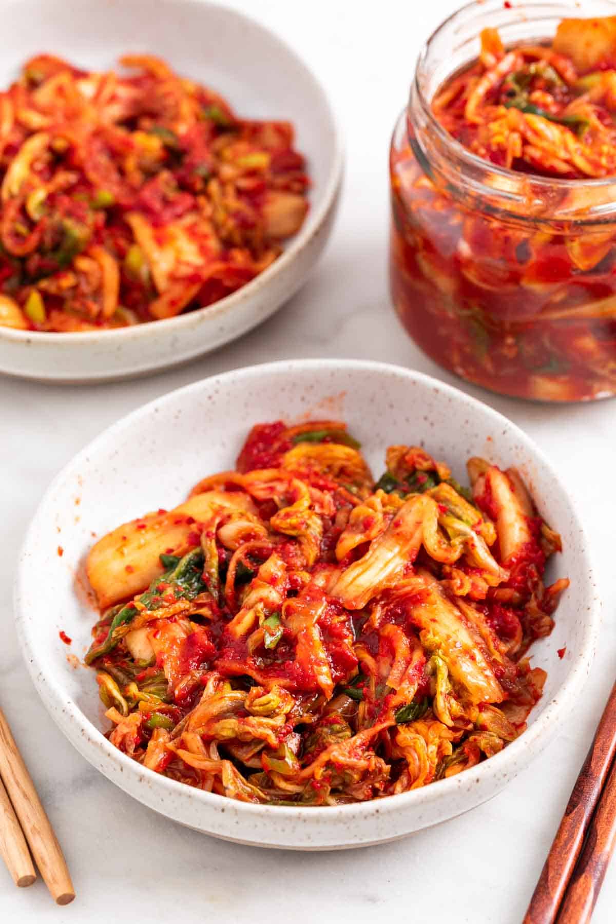 Vegan kimchi in two shallow dishes and in a jar.