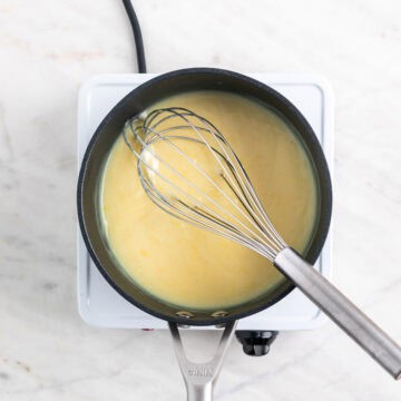 Vegan lemon curd in a saucepan with a whisk inside, before adding food coloring and butter