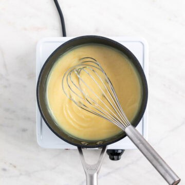 Vegan lemon curd in a saucepan with a whisk inside, before adding food coloring.