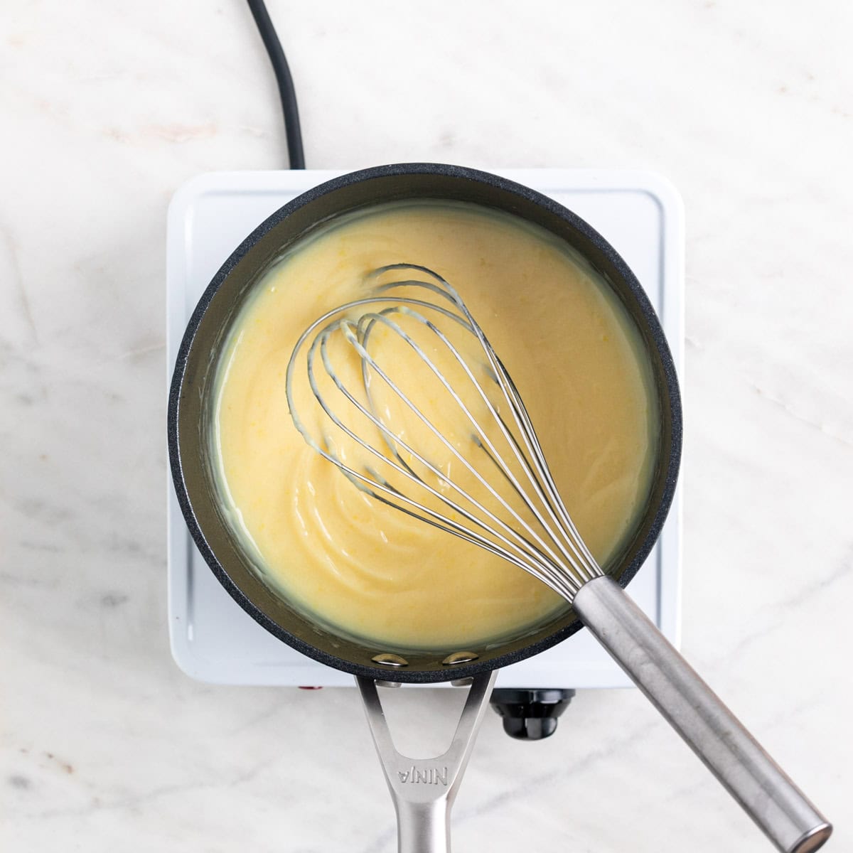 Vegan lemon curd in a saucepan with a whisk inside, before adding food coloring.
