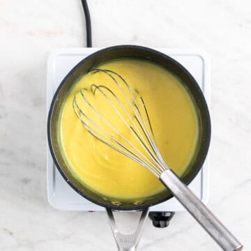 Vegan lemon curd in a saucepan with a whisk inside.