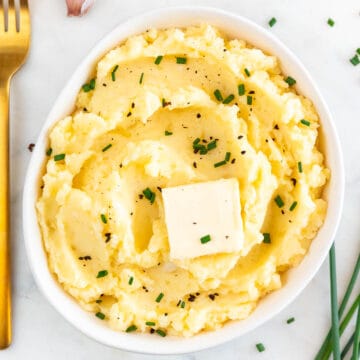 Bowl of vegan mashed potatoes with vegan butter, chives, and black pepper garnish and a fork.