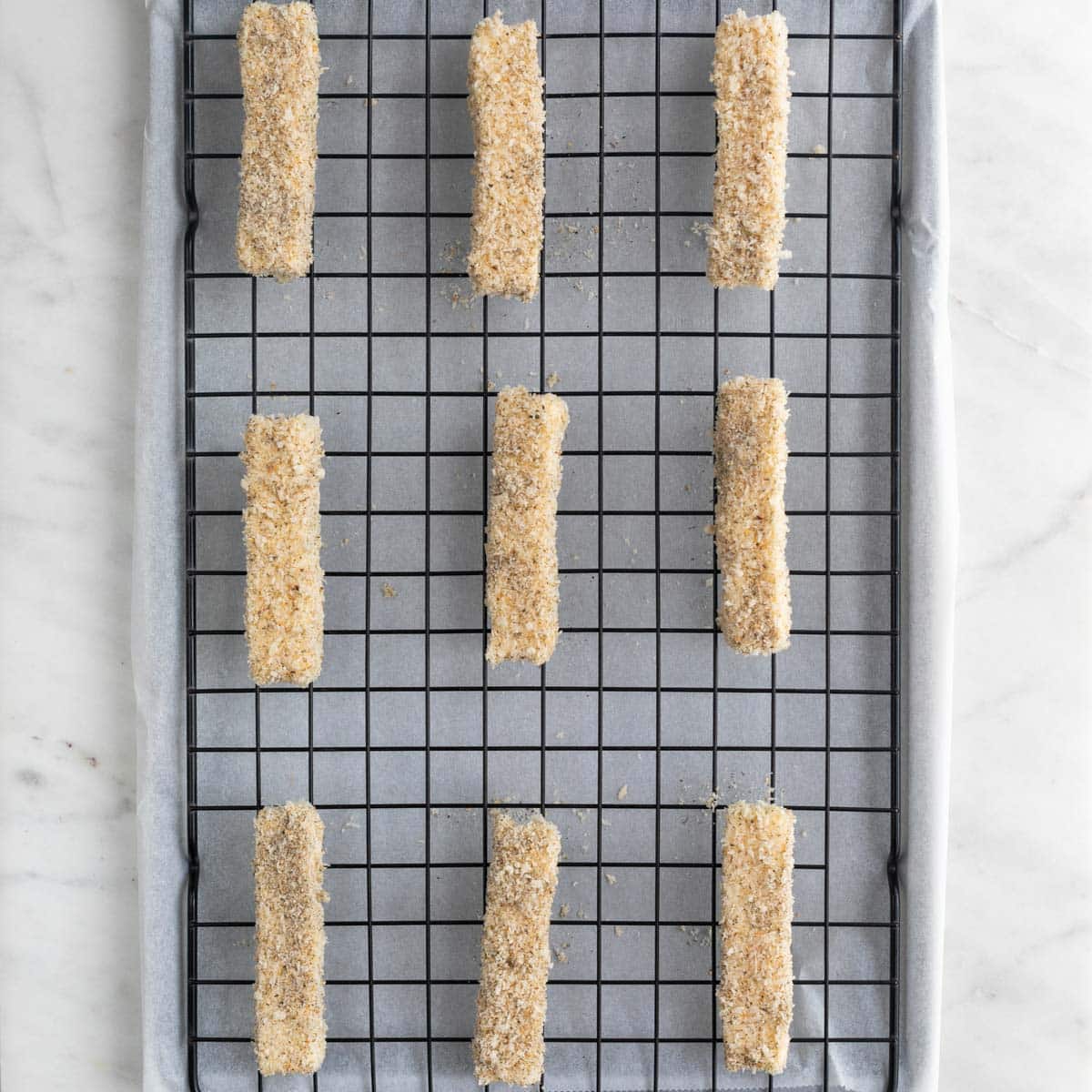 Vegan mozzarella sticks on a wire rack on a lined baking sheet before cooking.