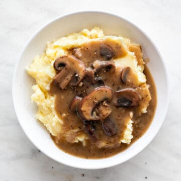 Platter featuring vegan mashed potatoes and vegan mushroom gravy against a white backdrop.